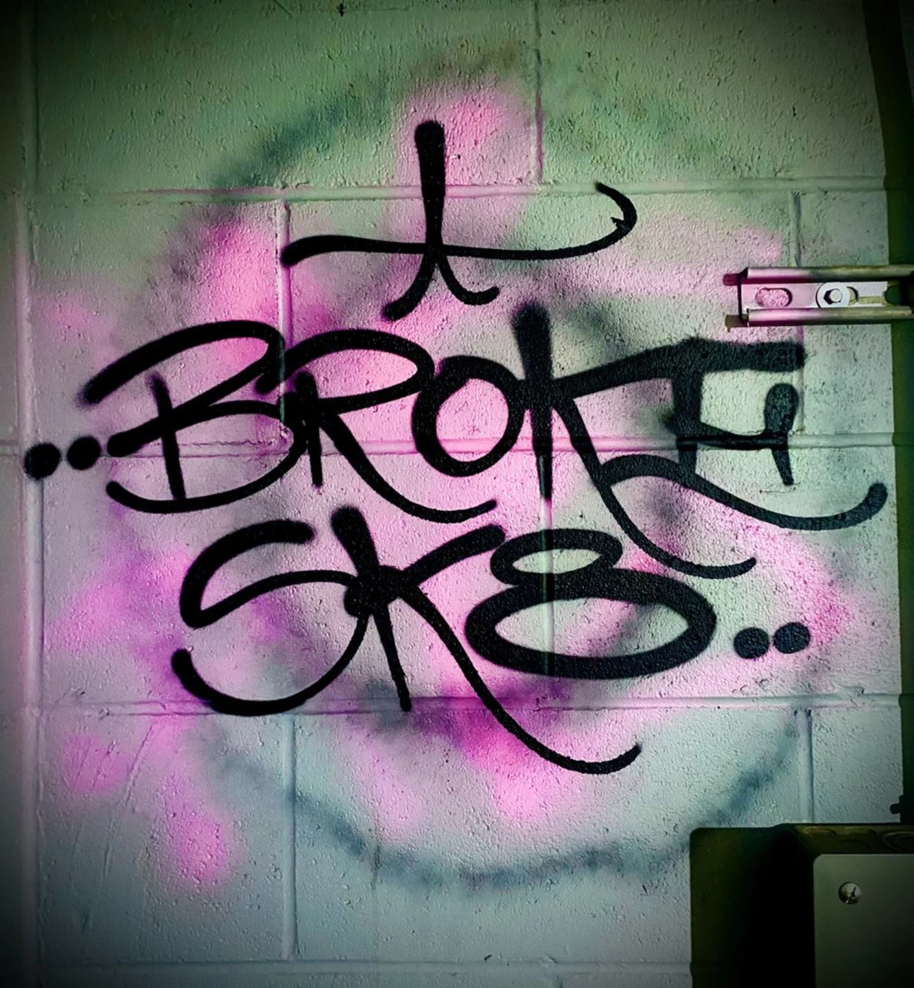 Black Broke Sk8 tag over pink and purple spray paint on a cinder block wall